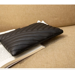Detail of black quilted leather clutch bag with golden metal trim and V-shaped stitching