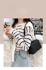 Modern black quilted crossbody bag with golden chain strap on a model in a cafe