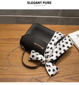Detail of black textured leather bag with gold chain strap and polka dot silk scarf