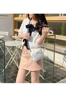 Close-up of white wave quilted crossbody bag with golden hardware and printed strap