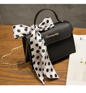 Close-up of black leather bag with gold logo, chain strap, and polka dot bow detail