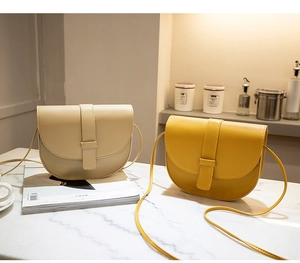 Detail of minimalist saddle crossbody bags in beige and yellow on marble surface