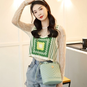 Detail of mint green quilted bucket bag with gold chain strap worn by a female model