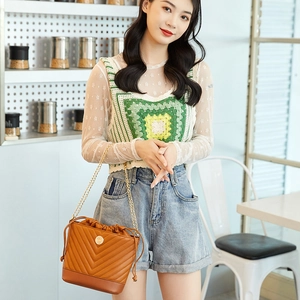 Brown quilted leather bucket bag featuring a gold chain strap worn by a model indoors