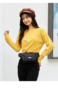 Detail of a black quilted waist bag with gold hardware worn by a model in yellow sweater