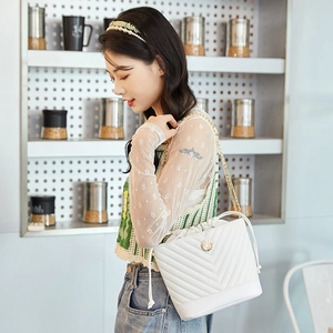 Close-up of white quilted bucket bag featuring V-shaped stitching and gold chain strap