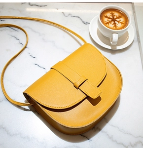 Top-down view of mustard yellow saddle bag on white marble next to a cup of coffee