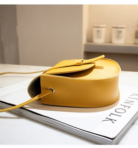 Detail of bright yellow saddle crossbody bag showing metal eyelet and slim leather strap