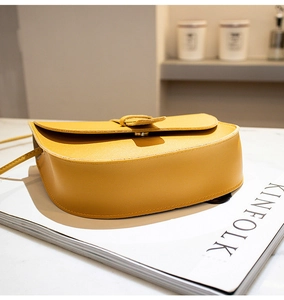 Detail of yellow PU leather saddle bag with lychee texture on marble and magazine