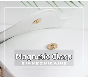 Close-up of the white leather bag featuring a gold magnetic snap button closure detail