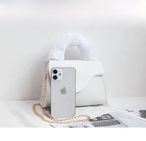 Detail of white mini crossbody bag with plush handle and chain strap beside a phone