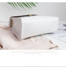 Detailed side view of white faux leather crossbody bag with golden chain and round metal clasp