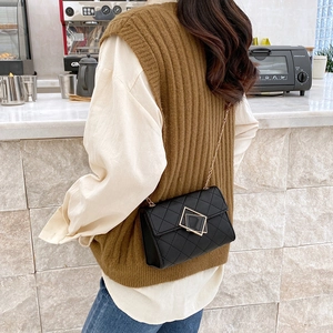 Schwarze gesteppte Umhängetasche mit goldener Kette, getragen von einem Modell im Café