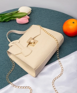Macro detail of beige croco embossed texture and gold heart-shaped metal lock on handbag