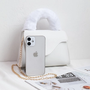 White mini crossbody bag with plush handle and gold chain next to a mobile phone