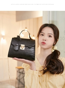 Detail of black crocodile pattern bag with gold clasp and chain in a cafe setting