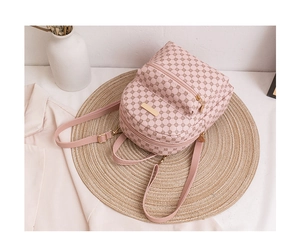 Detail eines rosa Mini-Rucksacks mit geometrischem Muster und goldener Hardware auf Stroh