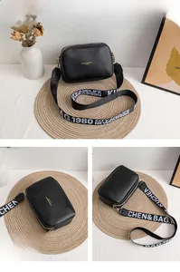Detail of black leather square bag with gold lettering and branded wide crossbody strap