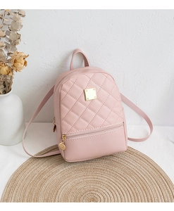 Pink quilted faux leather mini backpack on a rustic woven mat with floral decor