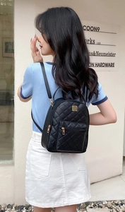Detail of black quilted mini backpack featuring gold metal plate and zipper on model