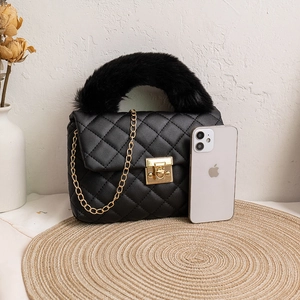 Black quilted crossbody bag with faux fur handle and golden chain strap on a woven mat