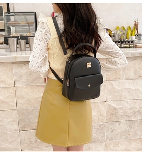 Model wearing a black mini leather backpack with metal detail in a cafe setting