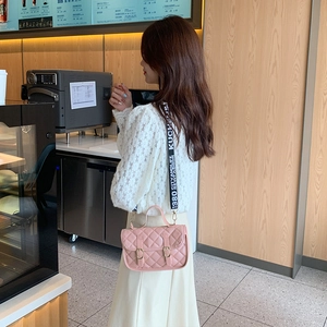 Pink quilted crossbody bag with a wide branded shoulder strap shown in a cafe setting