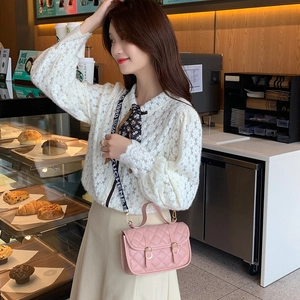 Pink quilted crossbody bag with patterned wide strap and gold hardware in cafe setting