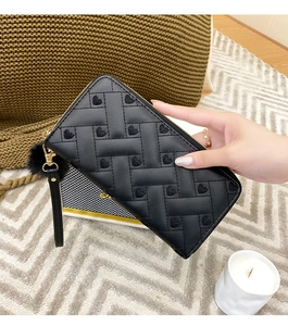 Close-up of black quilted long wallet with heart embroidery and fluffy pompom charm