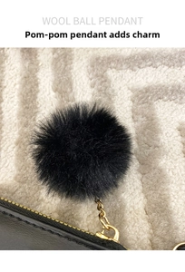 Detail shot of a black fluffy wool ball pendant with gold metal chain on a black leather bag