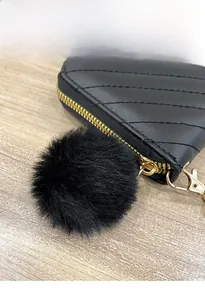 Detail view of black quilted leather purse with golden zipper and fluffy wool ball pendant