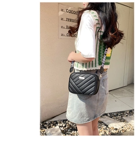 Detail of black leather crossbody bag with V-quilted texture and wide logo strap
