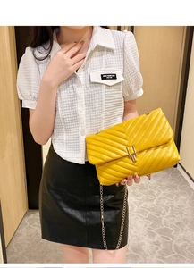 Detail of yellow quilted V-pattern handbag with gold chain strap worn by a model