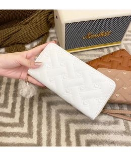 Detailed close-up of a long embroidered wallet with heart patterns and pompom charm