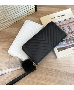 Detail of long quilted wallet with V-pattern stitching, fur pom-pom and wrist strap