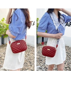 Detail of red quilted crossbody bag with golden plaque and patterned wide strap