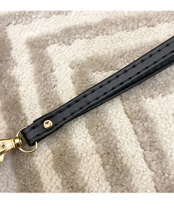 Close-up of black leather strap featuring gold metal lobster clasp and neat stitching