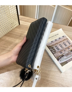 Close-up of quilted wallets in black and white with gold hardware and pompom charms