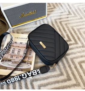 Detail of black quilted crossbody bag with a wide lettered strap on a chic textured rug