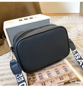 Detail of black rectangular camera bag with wide lettered strap on a textured rug