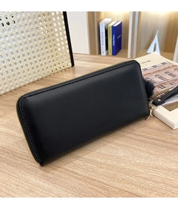 Detail of black V-quilted long wallet with golden zipper, wrist strap and plush pompom