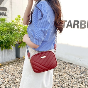 Red quilted camera bag with a wide lettered strap shown on a model in a street style shot