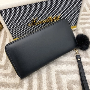 Elegant black leather zip wallet with wrist strap and faux fur pompom on textured rug