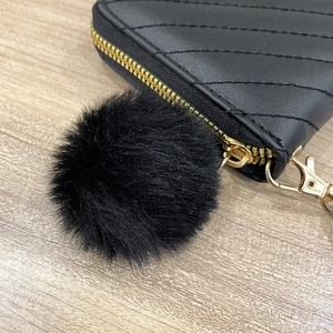 Black quilted clutch wallet with gold zipper and a fluffy faux fur pompom keychain