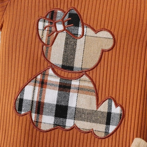 Détail d'un body bébé avec une applique d'ours et des motifs à carreaux