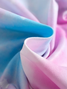 Detailed close-up of rainbow gradient tie-dye fabric with soft pink and blue pastel tones