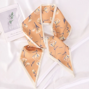 Floral print orange narrow silk scarf styled in a loop on white satin background