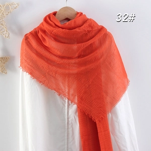 Détail d'une écharpe orange en coton et lin avec texture froissée et bords effilochés