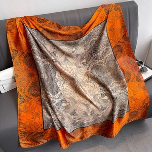 Carré de soie 110cm imprimé jungle orange posé sur un canapé en cuir gris
