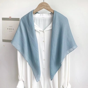 Detail of light blue minimalist scarf draped over a white shirt on a wooden hanger